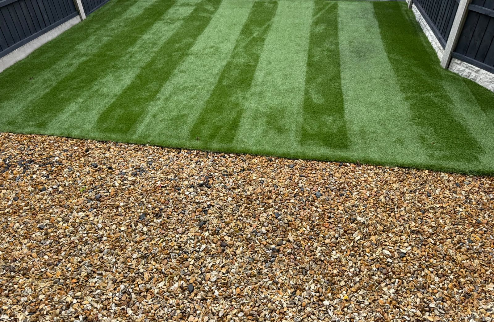 Artificial lawn after cleaning, with crisp brushed stripes running the length of the garden beside a gravel border