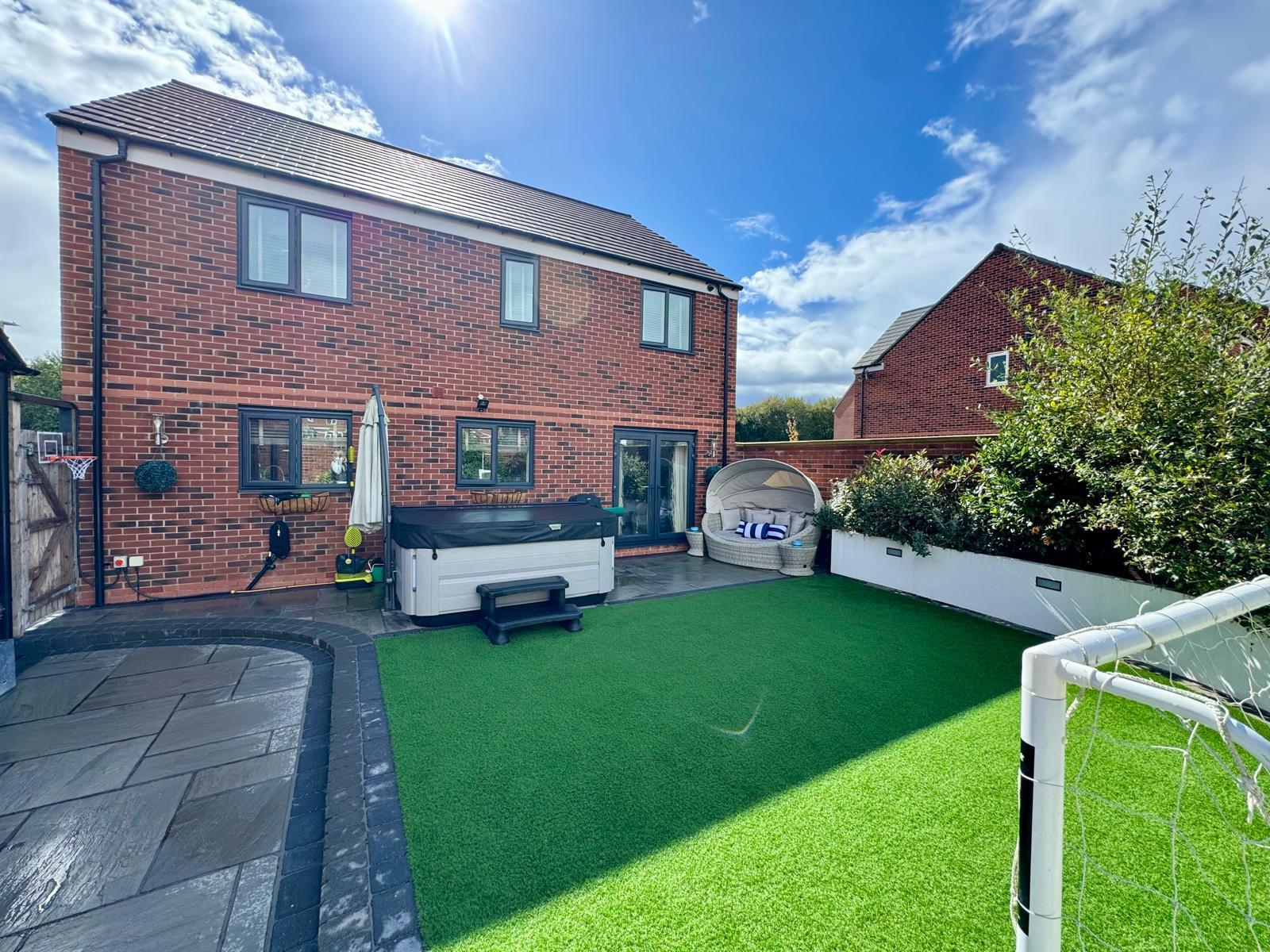 The same rear garden after deep cleaning, with a clear, vibrant artificial lawn, patio, hot tub and football goal fully reclaimed