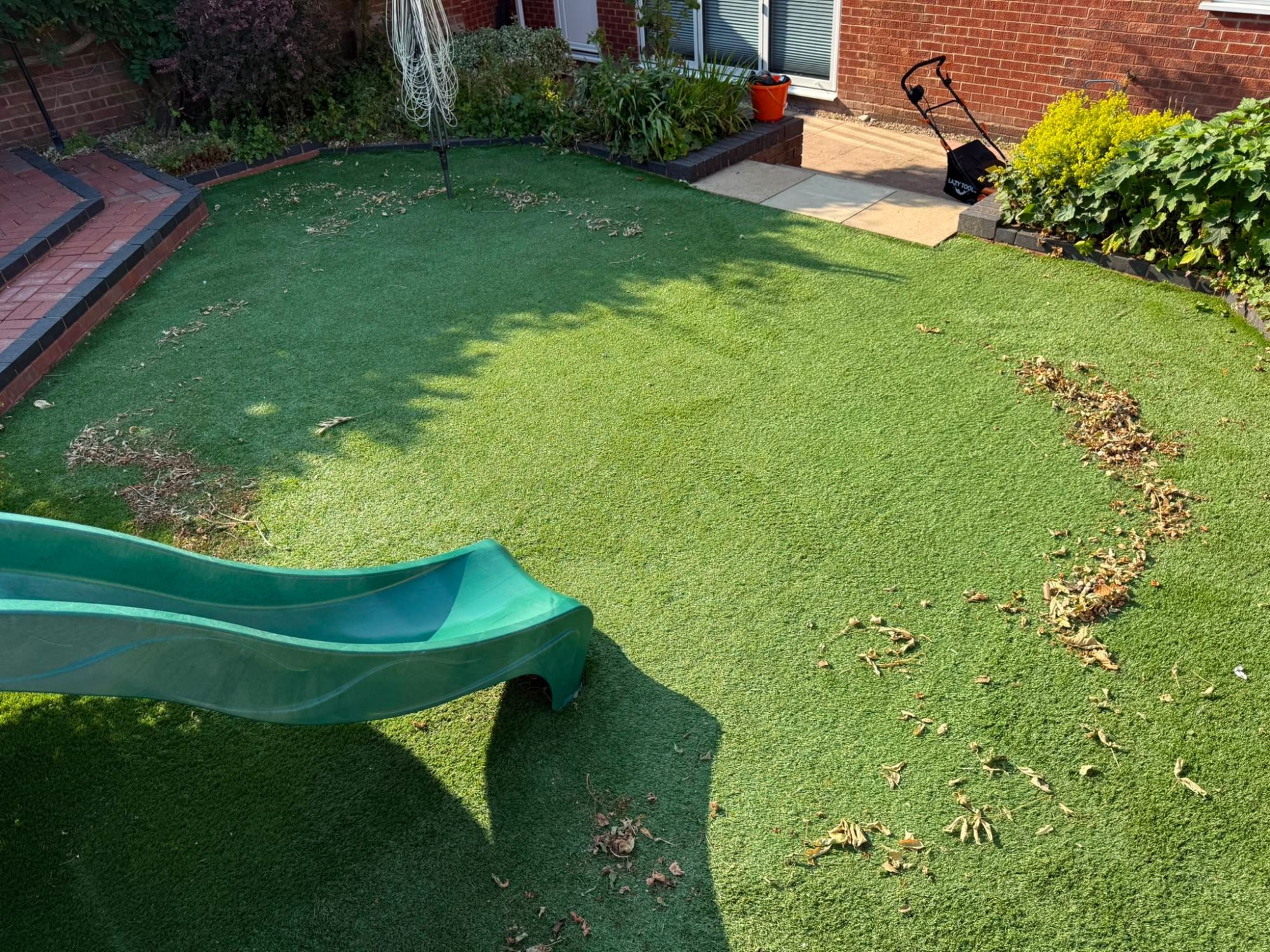 Artificial lawn scattered with hedge trimmings and dead leaves before clearing and brushing